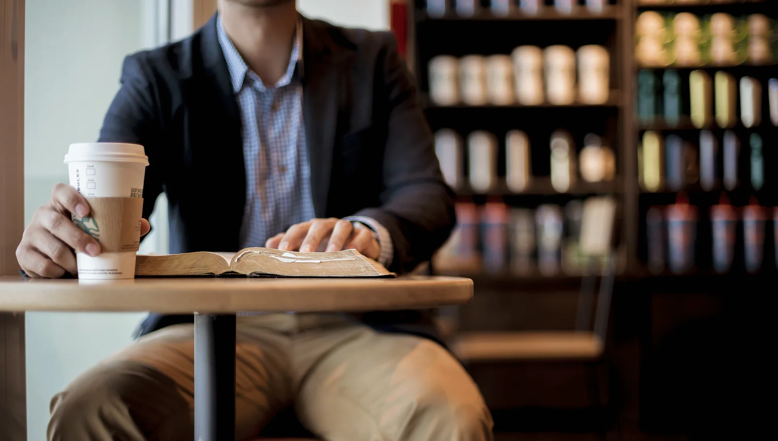 مردی در حال خوردن قهوه و خواندن کتاب در کافه